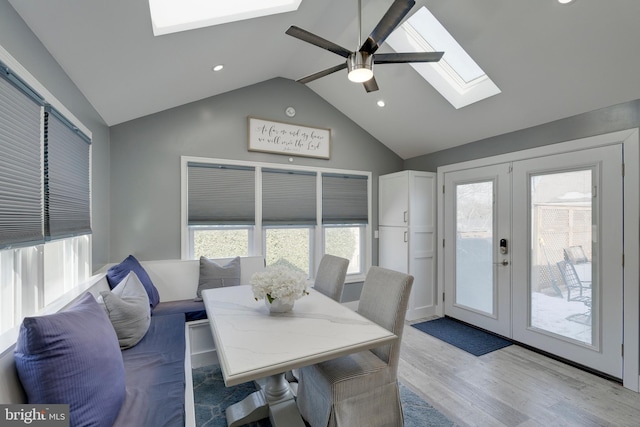 dining room with light wood-type flooring, vaulted ceiling with skylight, a wealth of natural light, and french doors