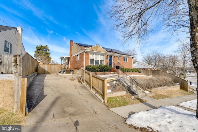 view of front of property featuring roof mounted solar panels, brick siding, and fence