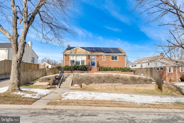 ranch-style house featuring a chimney, roof mounted solar panels, fence, and brick siding