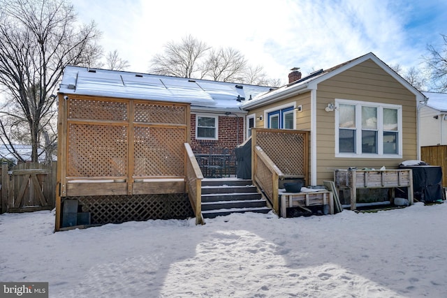 snow covered house featuring a chimney, fence, and a deck