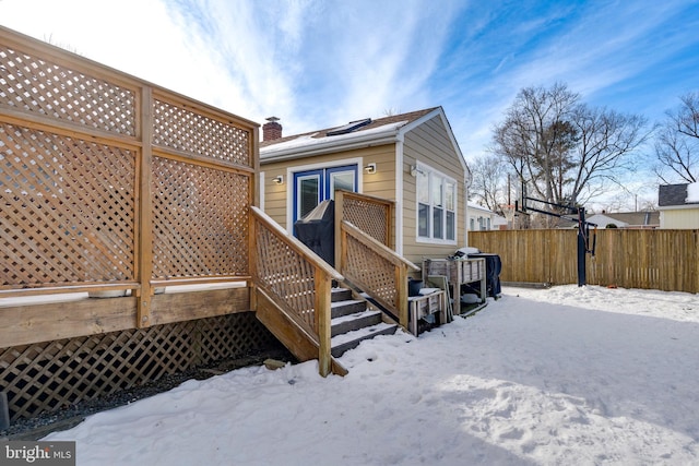 snow covered rear of property with a chimney and fence