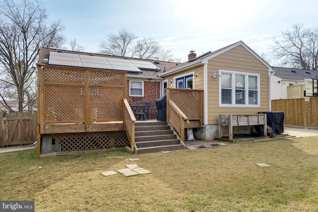 rear view of house with roof mounted solar panels, fence, a wooden deck, and a lawn