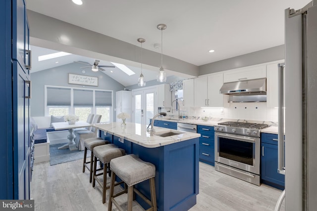 kitchen featuring under cabinet range hood, a sink, blue cabinetry, lofted ceiling with skylight, and high end appliances