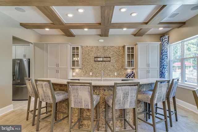 kitchen featuring tasteful backsplash, stainless steel refrigerator with ice dispenser, a large island with sink, and white cabinetry