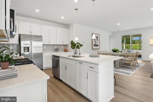 kitchen with a center island with sink, pendant lighting, sink, stainless steel appliances, and white cabinets