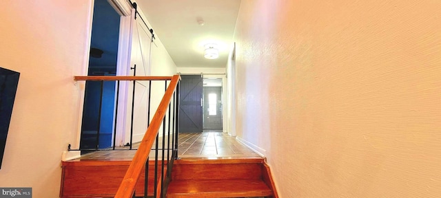 staircase with a barn door and tile patterned flooring