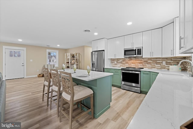 kitchen with a breakfast bar, sink, green cabinets, white cabinetry, and appliances with stainless steel finishes