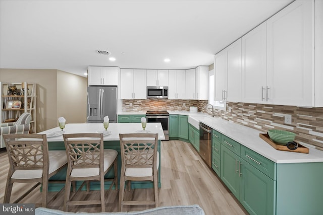 kitchen with white cabinets, appliances with stainless steel finishes, light hardwood / wood-style floors, backsplash, and green cabinetry