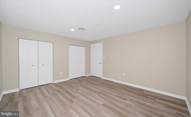 unfurnished bedroom featuring two closets and light wood-type flooring