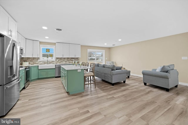 kitchen with appliances with stainless steel finishes, a kitchen breakfast bar, green cabinetry, a kitchen island, and sink