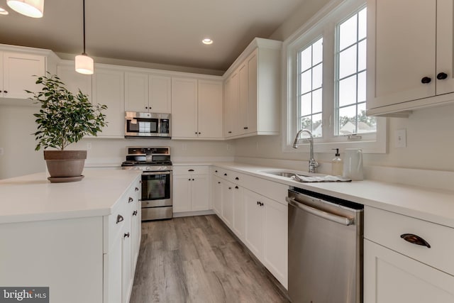 kitchen with decorative light fixtures, white cabinetry, stainless steel appliances, sink, and light hardwood / wood-style flooring