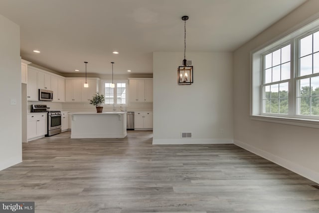 kitchen featuring white cabinetry, appliances with stainless steel finishes, hanging light fixtures, light hardwood / wood-style flooring, and a center island