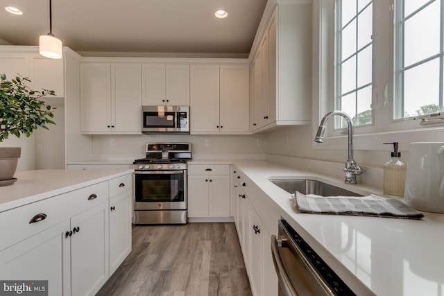 kitchen with pendant lighting, sink, light hardwood / wood-style flooring, stainless steel appliances, and white cabinets