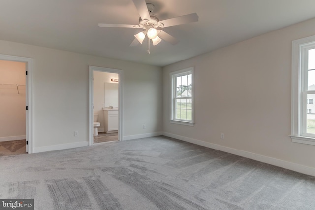 unfurnished bedroom featuring a spacious closet, connected bathroom, light carpet, a closet, and ceiling fan