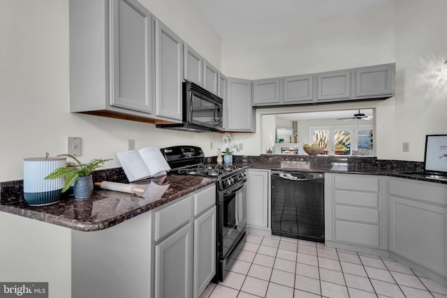 kitchen with black appliances, dark stone countertops, gray cabinetry, light tile patterned floors, and kitchen peninsula