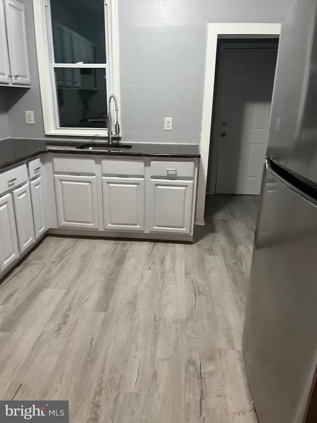 kitchen with light wood-type flooring, sink, stainless steel refrigerator, and white cabinetry