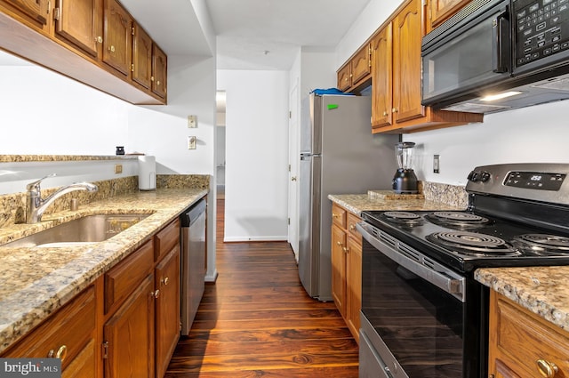 kitchen featuring light stone counters, brown cabinets, dark wood finished floors, appliances with stainless steel finishes, and a sink