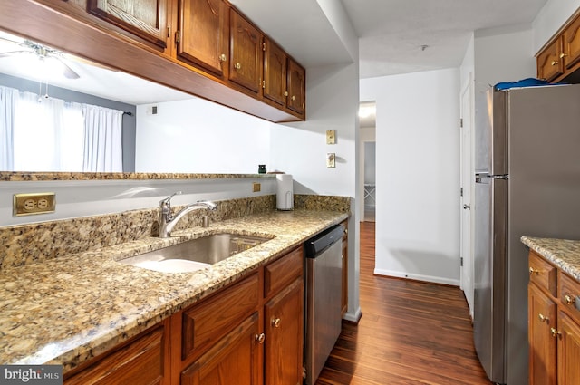 kitchen featuring light stone counters, brown cabinets, appliances with stainless steel finishes, dark wood-type flooring, and a sink