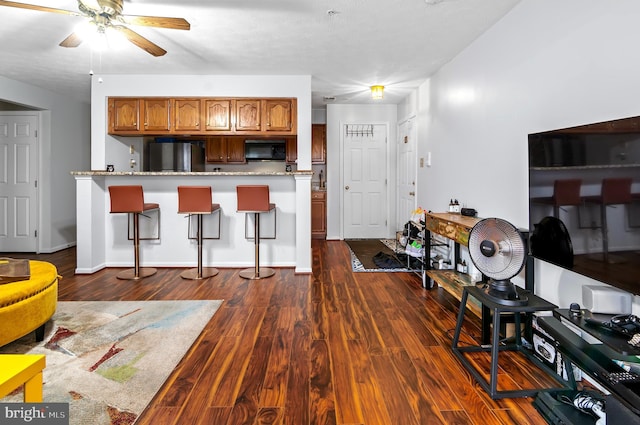 kitchen featuring brown cabinetry, dark wood finished floors, freestanding refrigerator, a kitchen bar, and black microwave