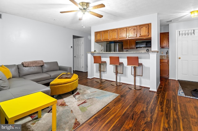 living area featuring dark wood-style floors, ceiling fan, visible vents, and baseboards