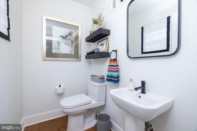 half bath with toilet, wood finished floors, baseboards, and a sink