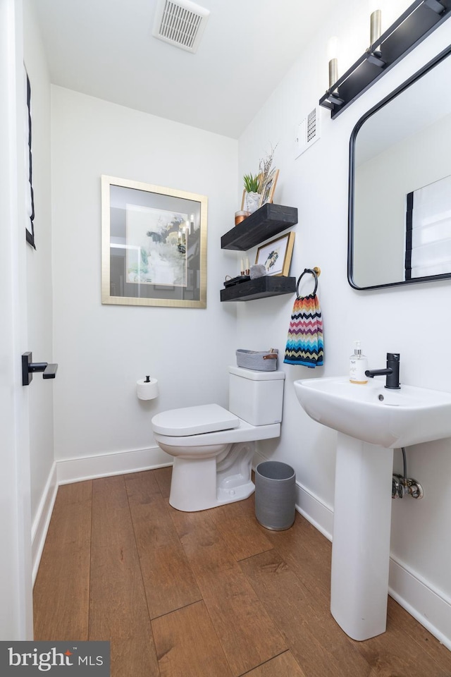 half bathroom with toilet, wood finished floors, visible vents, and baseboards