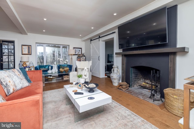 living area with recessed lighting, a barn door, a fireplace with flush hearth, and wood finished floors