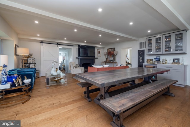 dining area featuring visible vents, light wood finished floors, beam ceiling, recessed lighting, and a barn door