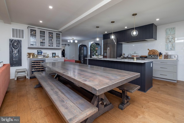 dining area featuring beverage cooler, visible vents, light wood finished floors, recessed lighting, and a bar