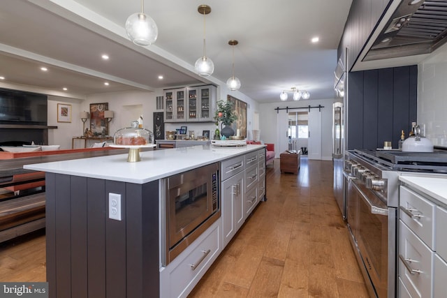 kitchen featuring premium appliances, open floor plan, a barn door, light wood-style floors, and wall chimney range hood