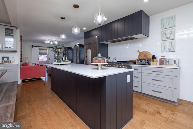 kitchen with a kitchen island, light countertops, light wood-type flooring, a barn door, and high quality fridge