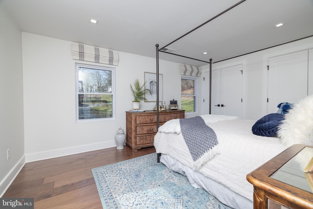 bedroom with multiple windows, wood finished floors, baseboards, and two closets