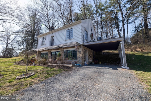 view of front of home featuring gravel driveway, a front lawn, stone siding, and a chimney