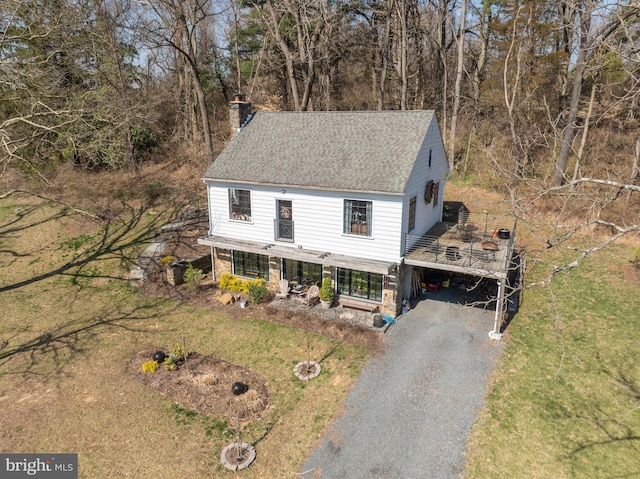 view of front of property with roof with shingles, a front yard, a chimney, stone siding, and driveway