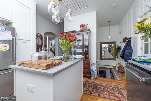 kitchen featuring wood finished floors, arched walkways, freestanding refrigerator, light countertops, and white cabinetry