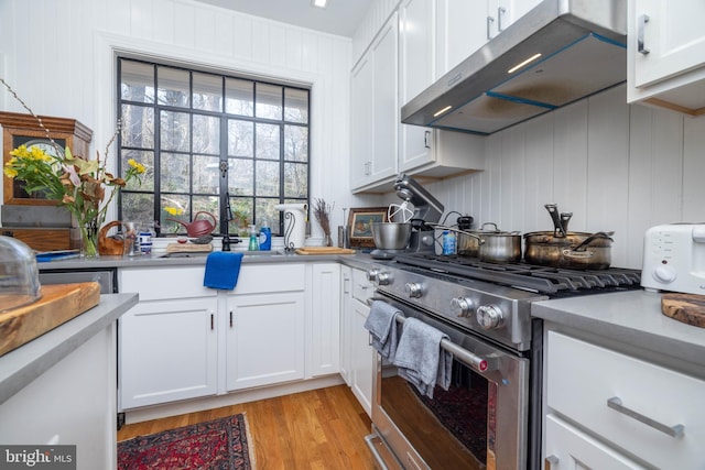 kitchen featuring light wood finished floors, high end stove, light countertops, white cabinets, and under cabinet range hood