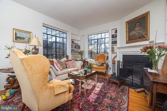 living room with built in shelves, wood finished floors, and a fireplace