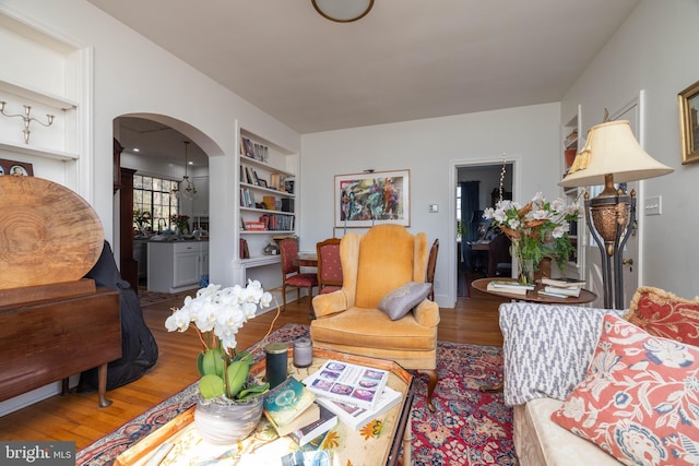 living area with built in shelves, arched walkways, and wood finished floors