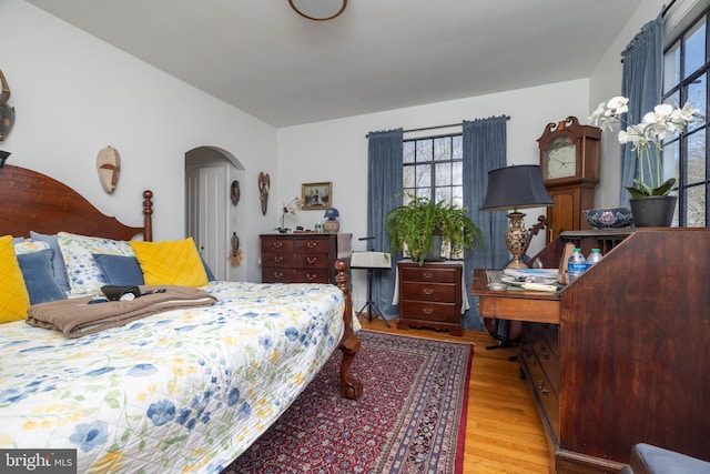 bedroom with vaulted ceiling, wood finished floors, and arched walkways