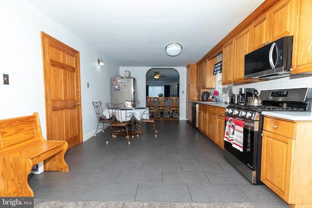 kitchen with dark tile patterned flooring, tasteful backsplash, ceiling fan, and appliances with stainless steel finishes