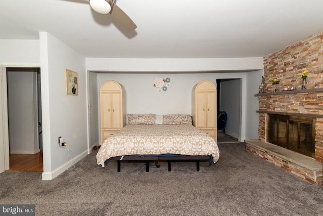 bedroom featuring ceiling fan, a large fireplace, and dark colored carpet