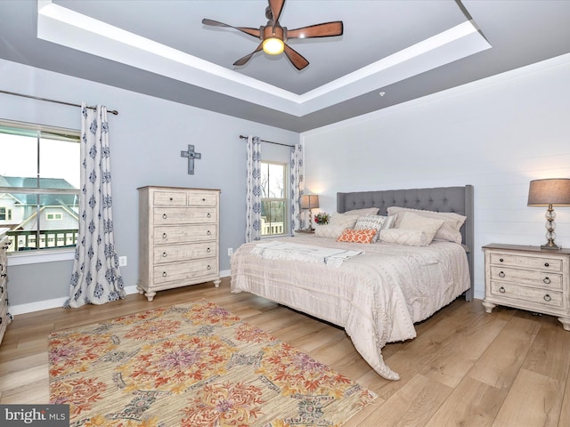 bedroom with hardwood / wood-style floors, ceiling fan, and a raised ceiling