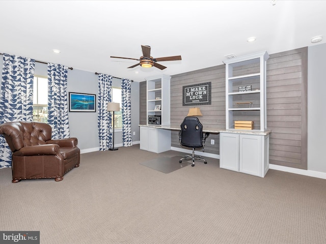 carpeted office space featuring built in desk, wood walls, and ceiling fan