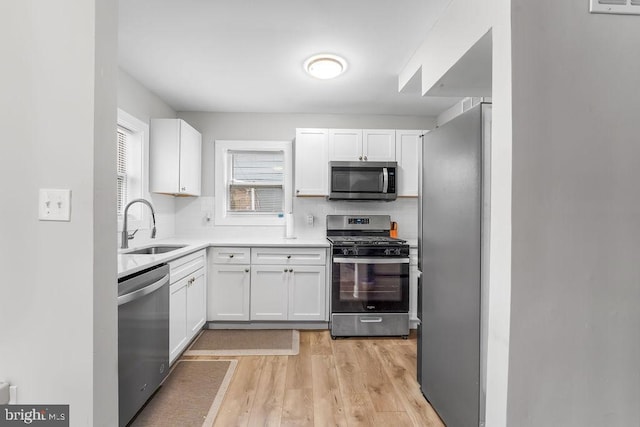 kitchen with tasteful backsplash, sink, white cabinetry, light hardwood / wood-style flooring, and appliances with stainless steel finishes