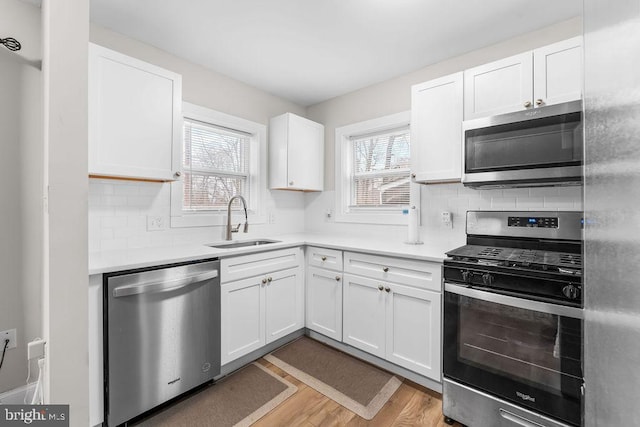 kitchen featuring white cabinets, appliances with stainless steel finishes, decorative backsplash, sink, and light wood-type flooring