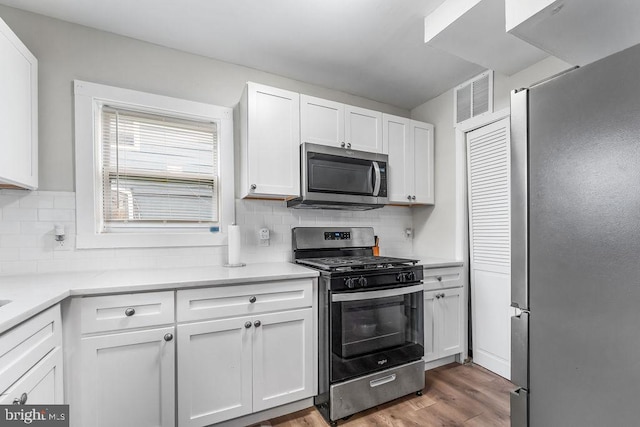 kitchen with hardwood / wood-style flooring, white cabinetry, appliances with stainless steel finishes, and tasteful backsplash