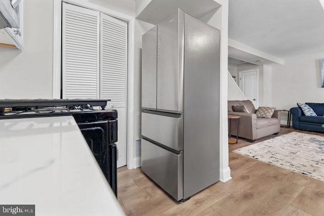 kitchen with light wood-type flooring, white cabinets, gas stove, and stainless steel fridge