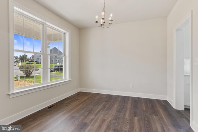 empty room with a notable chandelier, plenty of natural light, and dark hardwood / wood-style flooring