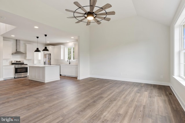 kitchen with appliances with stainless steel finishes, wall chimney exhaust hood, white cabinetry, hanging light fixtures, and vaulted ceiling