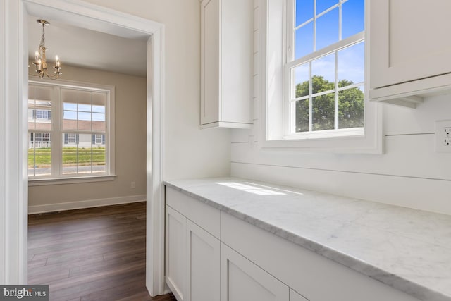 interior space featuring pendant lighting, white cabinetry, dark wood-type flooring, light stone counters, and a chandelier